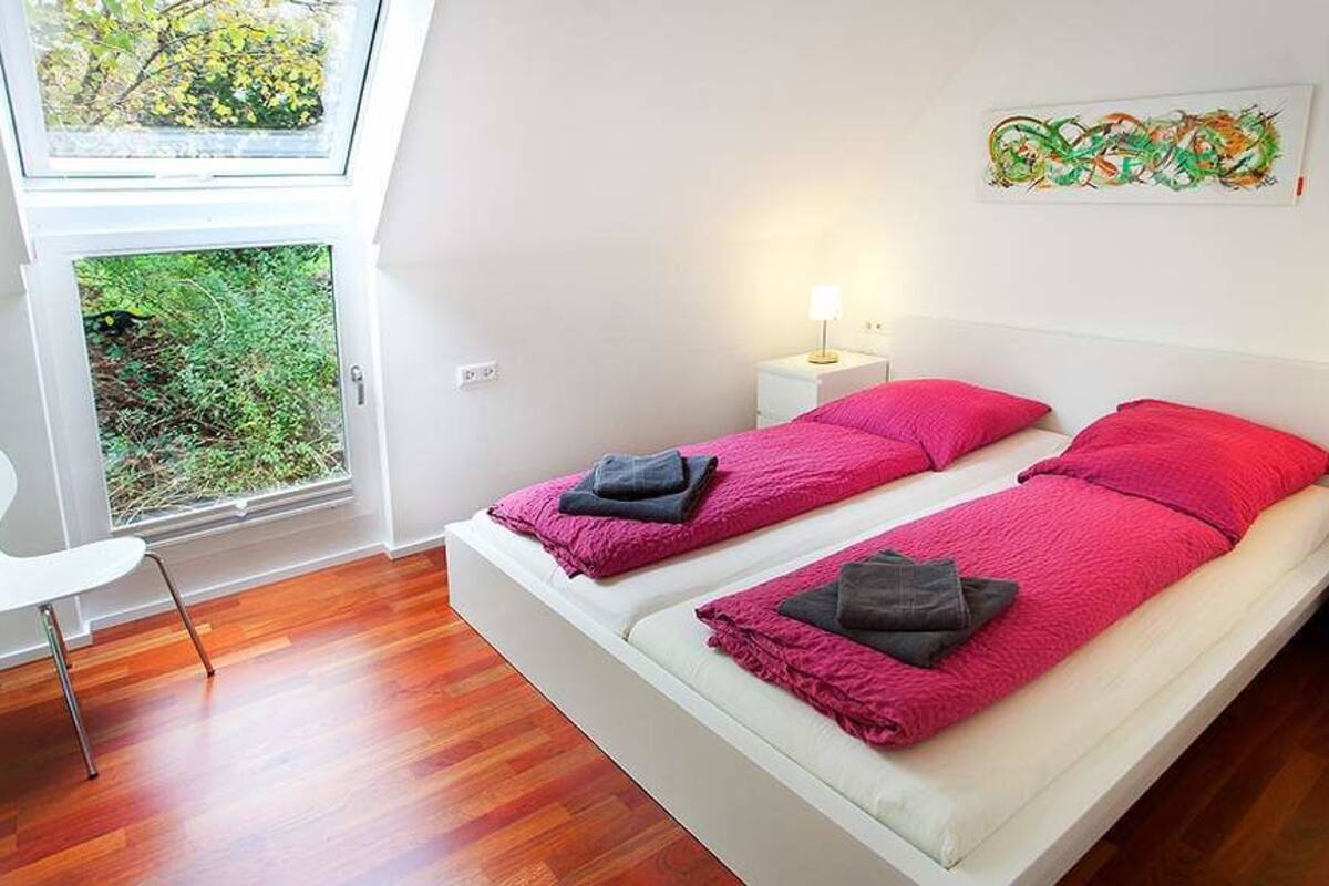 Ein Doppelbett mit rosa Bettwäsche, zwei Nachttische mit Lampen, ein Fenster mit Blick auf Grünflächen und ein Bild an der Wand.