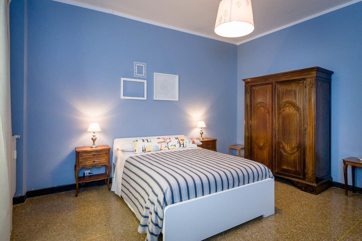 Un dormitorio con cama, dos mesitas de noche con lámparas, un armario y marcos de cuadros en la pared.