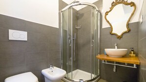 Un baño moderno con ducha envuelta en vidrio, inodoro blanco, bidé y tocador de madera con lavabo y espejo.