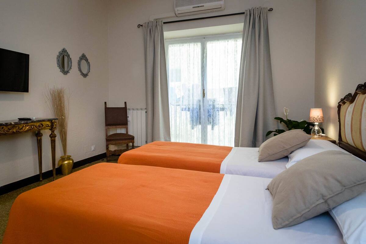 Habitación de hotel con dos camas, un escritorio, una silla y un ventanal con cortinas.
