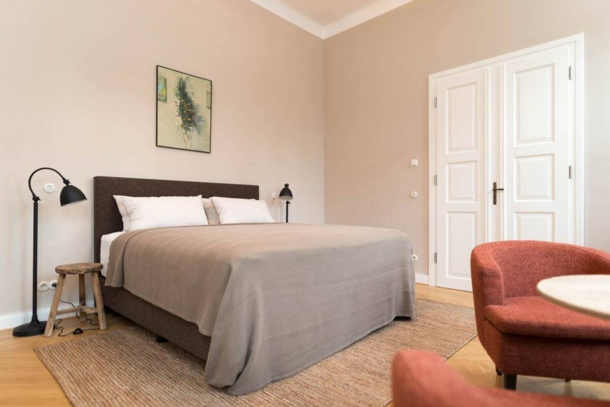 Une chambre à coucher avec un lit, des lampes de chevet, un petit tabouret, une chaise et une porte.