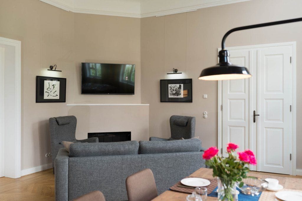 Ein modernes Wohnzimmer mit grauem Sofa, einem flachbildfernseher über einem Kamin und einem Esstisch, der mit Tellern und einer Blumenvase gedeckt ist.