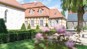 A traditional European-style building with a symmetrical facade, multiple windows, and a well-maintained garden with hedges and flowering plants. - Schloss Beuchow (Lübbenau/Spreewald)