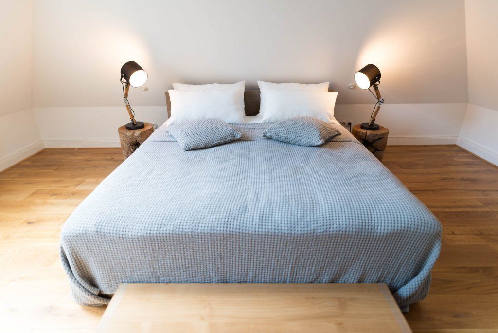 A neatly made bed with a checkered bedspread, two bedside lamps, and a wooden bench at the foot of the bed.