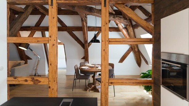 A rustic interior with exposed wooden beams, a dining area with chairs and a table set for four, and a kitchen area with modern appliances. - Schloss Beuchow (Lübbenau/Spreewald)