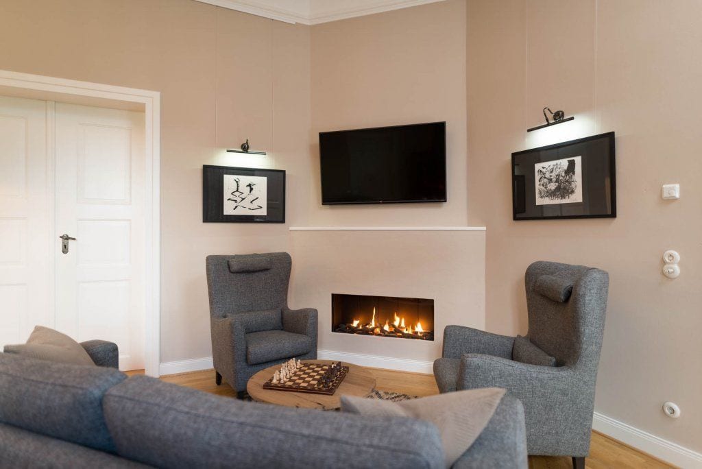 A living room with a fireplace, grey sofas, a flat-screen TV, and framed artwork on the walls.