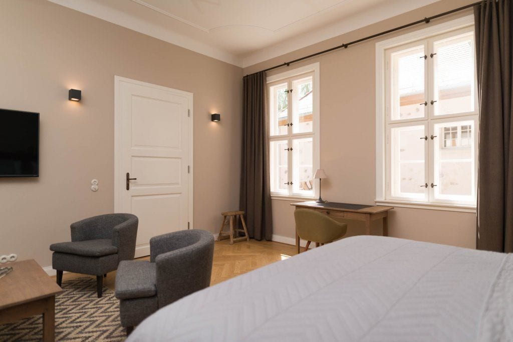 Une chambre d’hôtel avec un lit, un bureau, deux chaises, une télévision et une fenêtre avec des rideaux.