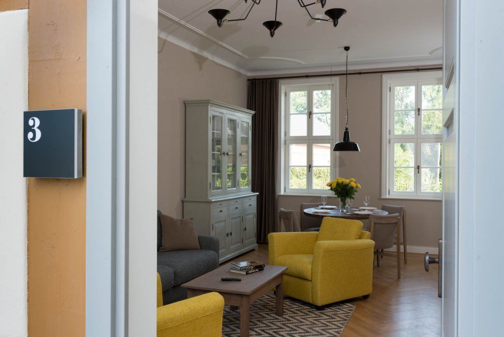 A living room with a sofa, yellow armchairs, a cabinet, and a dining area with a table and chairs.