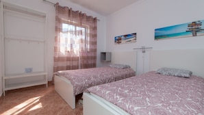Un dormitorio con dos camas, un armario, una cortina y dos cuadros colgados en la pared.