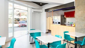 Een modern restaurantinterieur met witte tafels en teal stoelen, een houten toonbank en een uitzicht op de straat door grote glazen deuren.