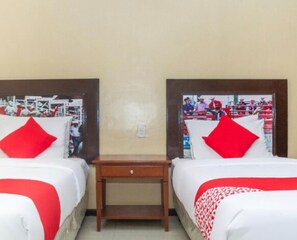 A hotel room with two beds, each with red and white bedding, a small wooden nightstand, and a wall-mounted TV displaying a sports event. - OYO 133 Jazzy James Country Hotel 2 (Davao)