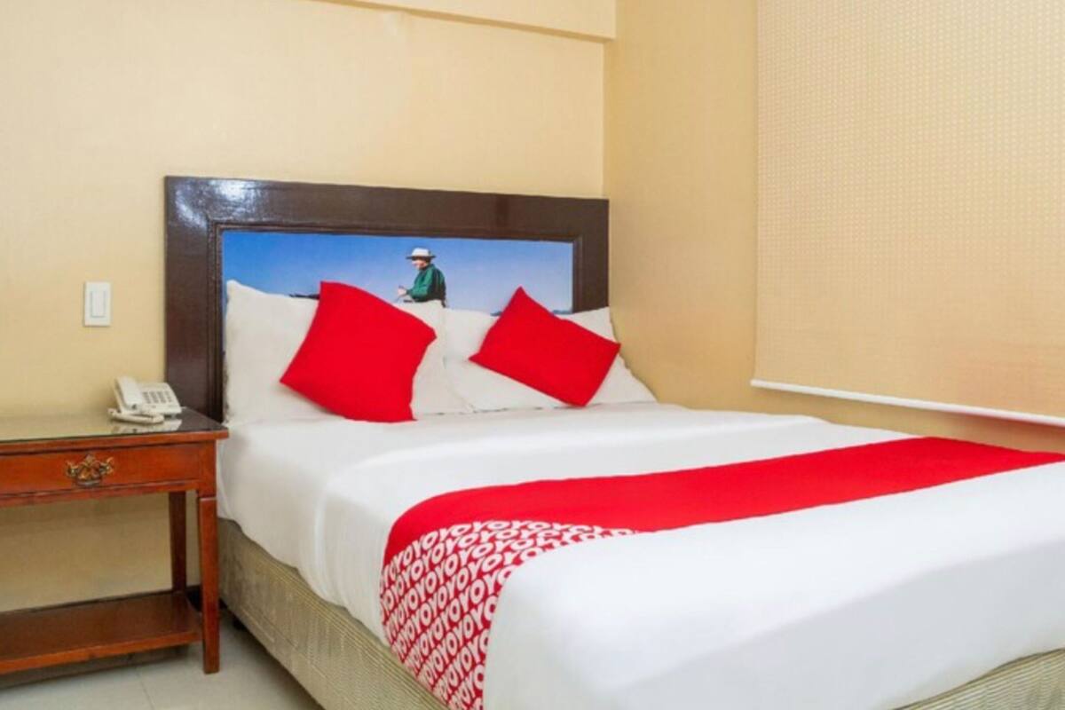 Ein Hotelzimmer mit einem Bett, einem Nachttisch, einem Telefon und einem Fenster mit Jalousien.