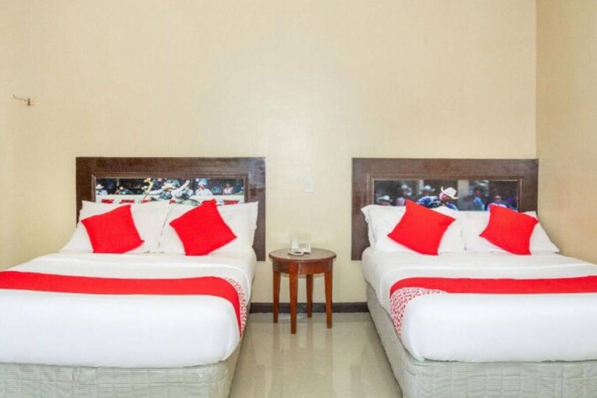 Ein Hotelzimmer mit zwei Betten, jeweils mit rot-weißer Bettwäsche, einem kleinen Holztisch und einer schlichten Wand.