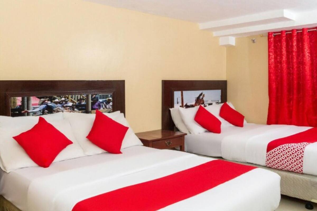 Ein Hotelzimmer mit zwei Betten, jeweils mit weißer Bettwäsche und roten Akzenten, einem Holz-Kopfteil und einem roten Vorhang.