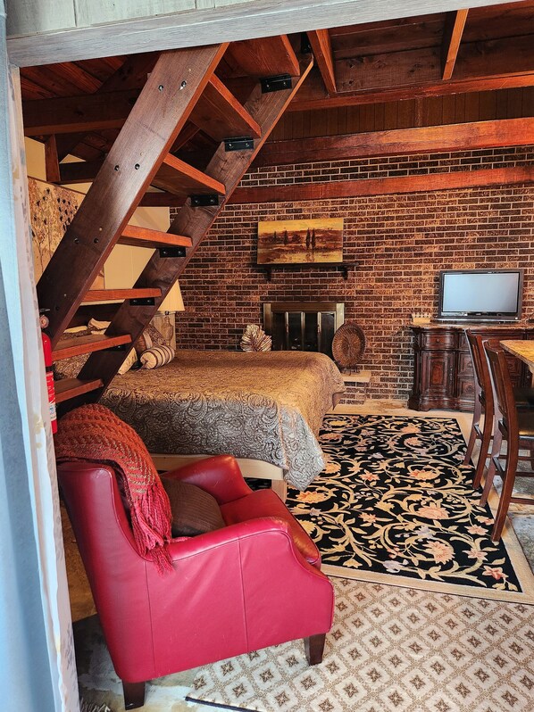 A rustic room with a loft bed, a red leather chair, a television, and a brick wall.