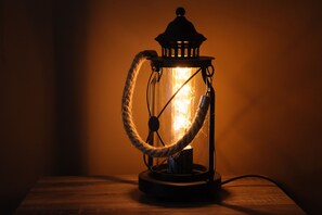 Een lamp met een lantaarnmodel en een touwen handgreep, bevestigd aan een houten oppervlak.
