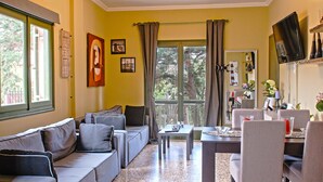 Un amplio espacio habitable con un conjunto de sofás, una mesa de comedor y sillas, un televisor y un gran ventanal con cortinas.