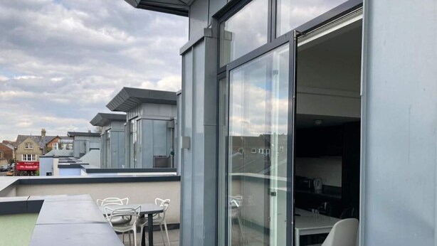 Eine Dachterrasse mit Essbereich, inklusive Tischen und Stühlen, und einer Glastür zum Innenbereich.
