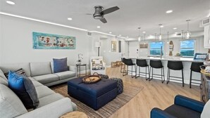 Uma sala de estar moderna com sofá, banquinho e um espaço de jantar com banquetas.