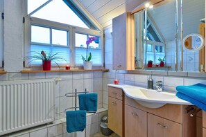 Ein modernes Badezimmer mit einem weißen Heizkörper, einem Waschbecken mit Spiegel und zwei blauen Handtüchern an einem Wäscheständer.