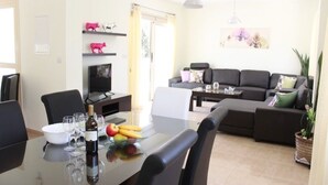 A dining area with a table set for six, a sofa, and a television. - Villa Ksenia (Paralimni)