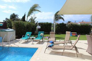 A pool area with lounge chairs, a pool ladder, and a covered seating area.