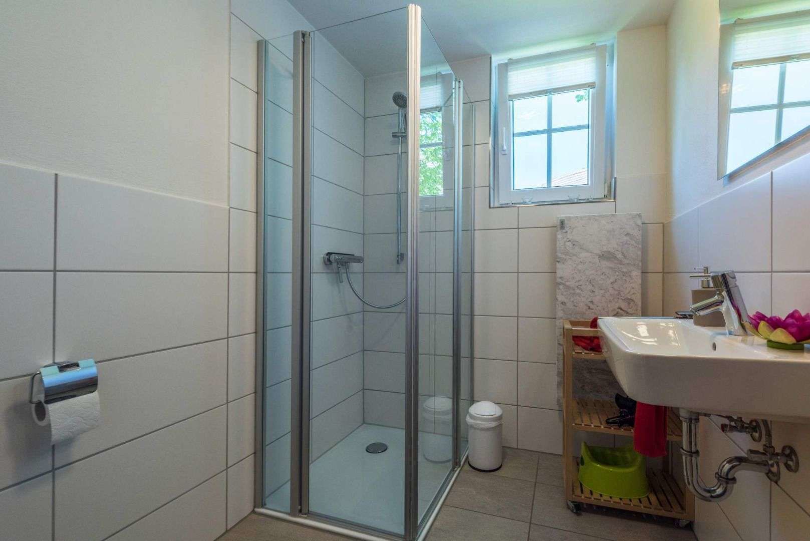 Ein modernes Badezimmer mit einer Duschkabine, einem Waschbecken mit Marmorplatte und einem Fenster für Tageslicht.