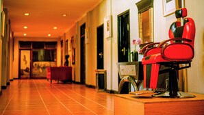 Un couloir d’hôtel avec un fauteuil de barbier rouge, un comptoir d’accueil en bois et un tableau encadré accroché au mur.