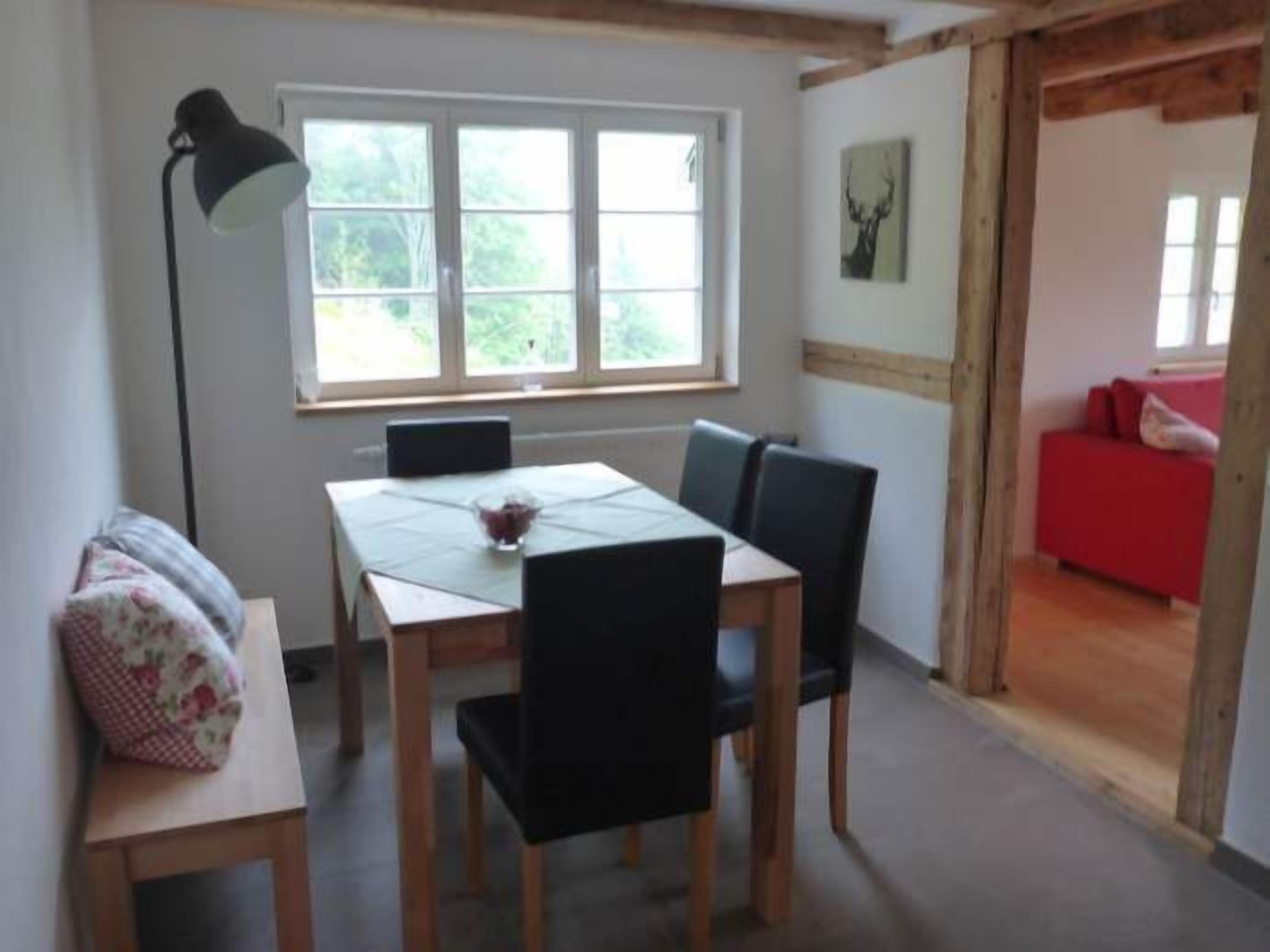 A dining area with a table and chairs, a lamp, and a window with a view of greenery.