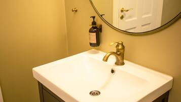 A white bathroom sink with a gold faucet, a soap dispenser, and a mirror above it.