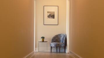 A hallway with a patterned chair, a small table with a plant, and a framed picture on the wall.