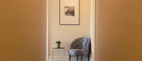 Un pasillo con una silla estampada, una mesita con una planta y un cuadro en la pared.