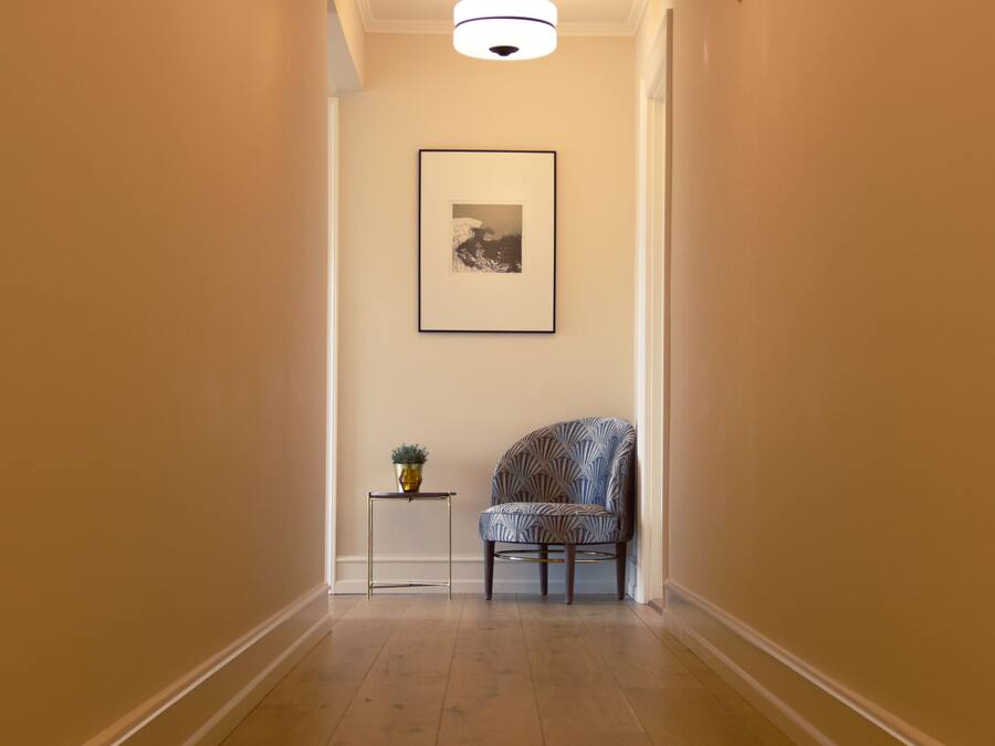 A hallway with a patterned chair, a small table with a plant, and a framed picture on the wall.