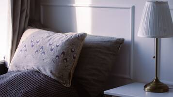 Una cama bien hecha con almohadas estampadas, una lámpara de noche y una ventana con cortinas.