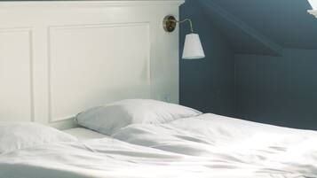 Un dormitorio con una cama blanca, una pared blanca y un techo inclinado.