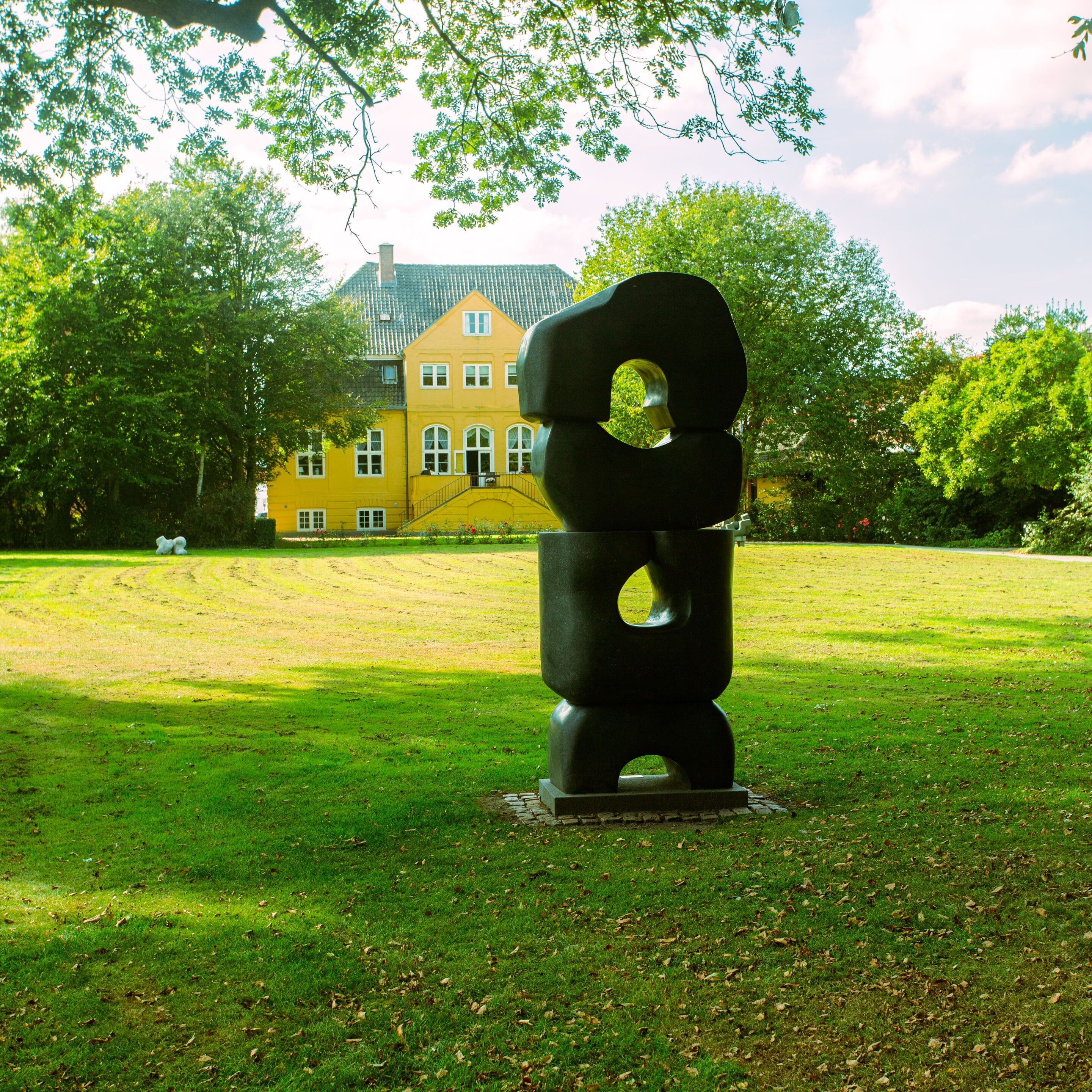 A sculpture in a park with a yellow building in the background.