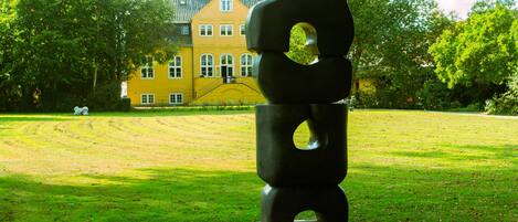 A sculpture in a park with a yellow building in the background.