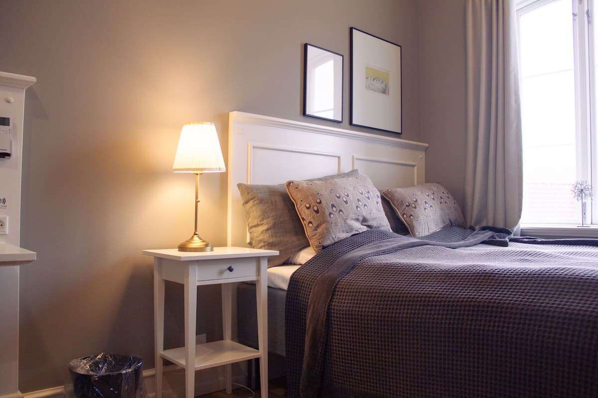 A neatly made bed with patterned bedding, a bedside lamp, and a small nightstand with a trash bin.