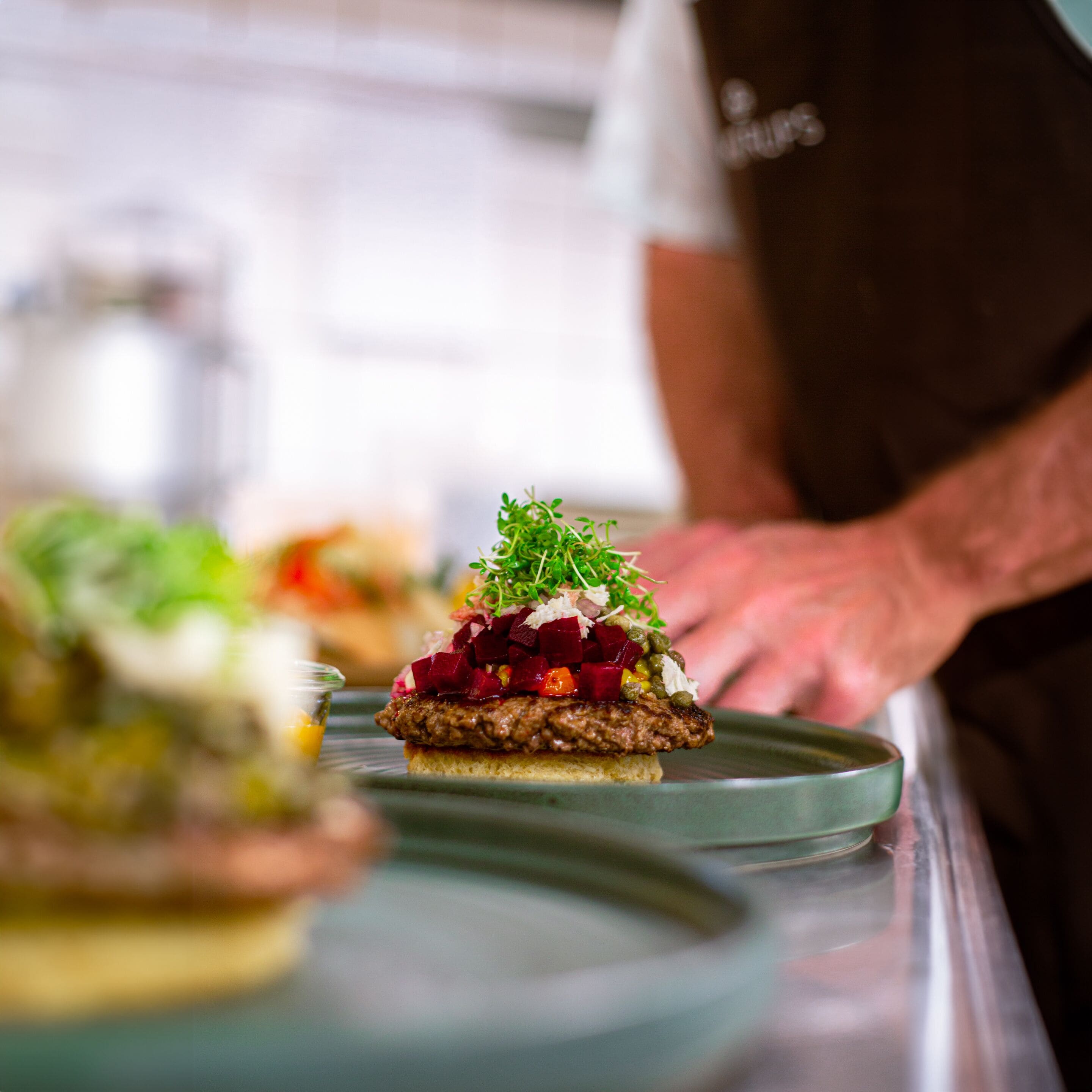 A close-up of a gourmet dish with a variety of toppings, including greens, beets, and possibly some type of cheese or sauce, served on a slice of bread.
