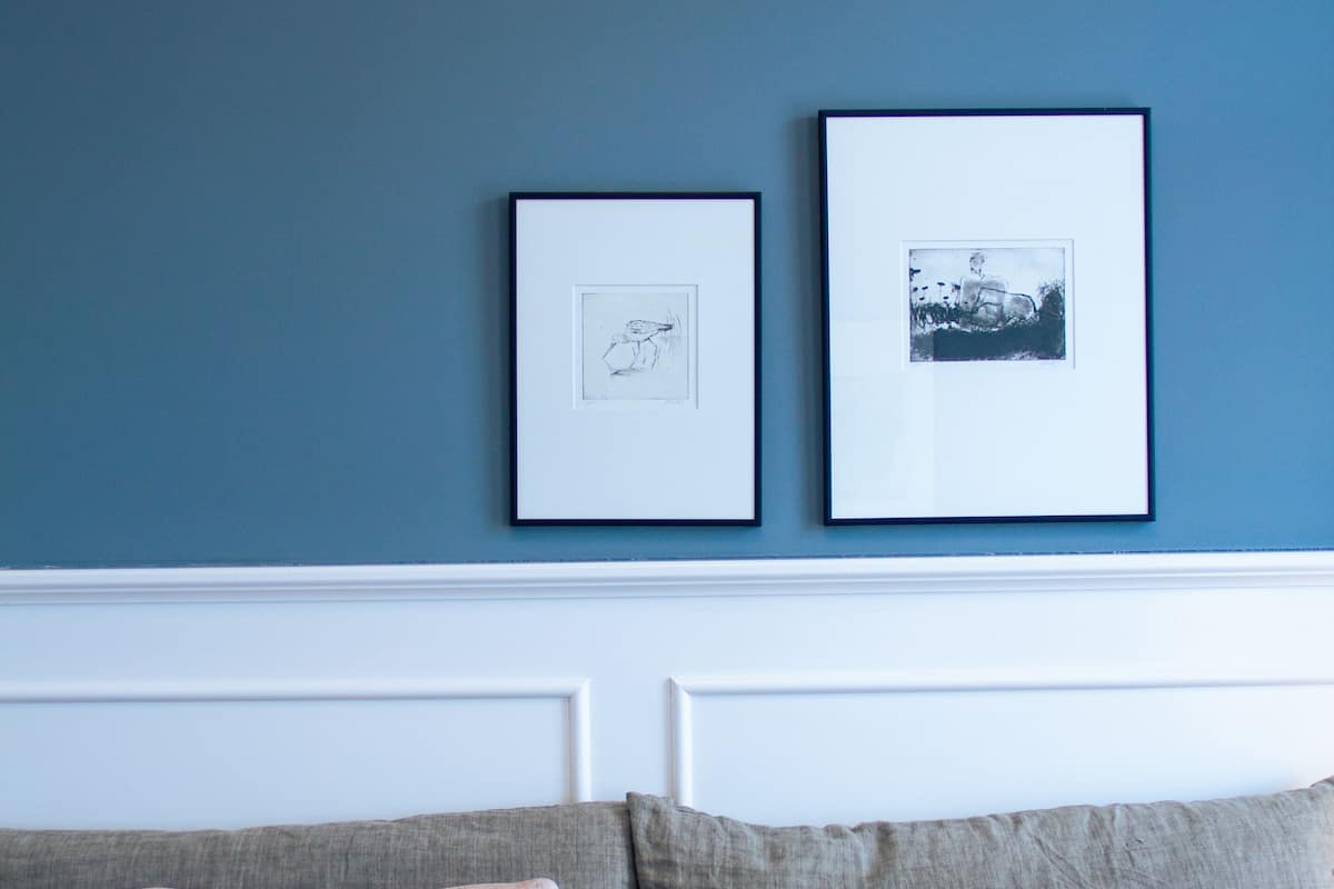 A bedroom with a bed, two pillows, and two framed pictures on the wall.