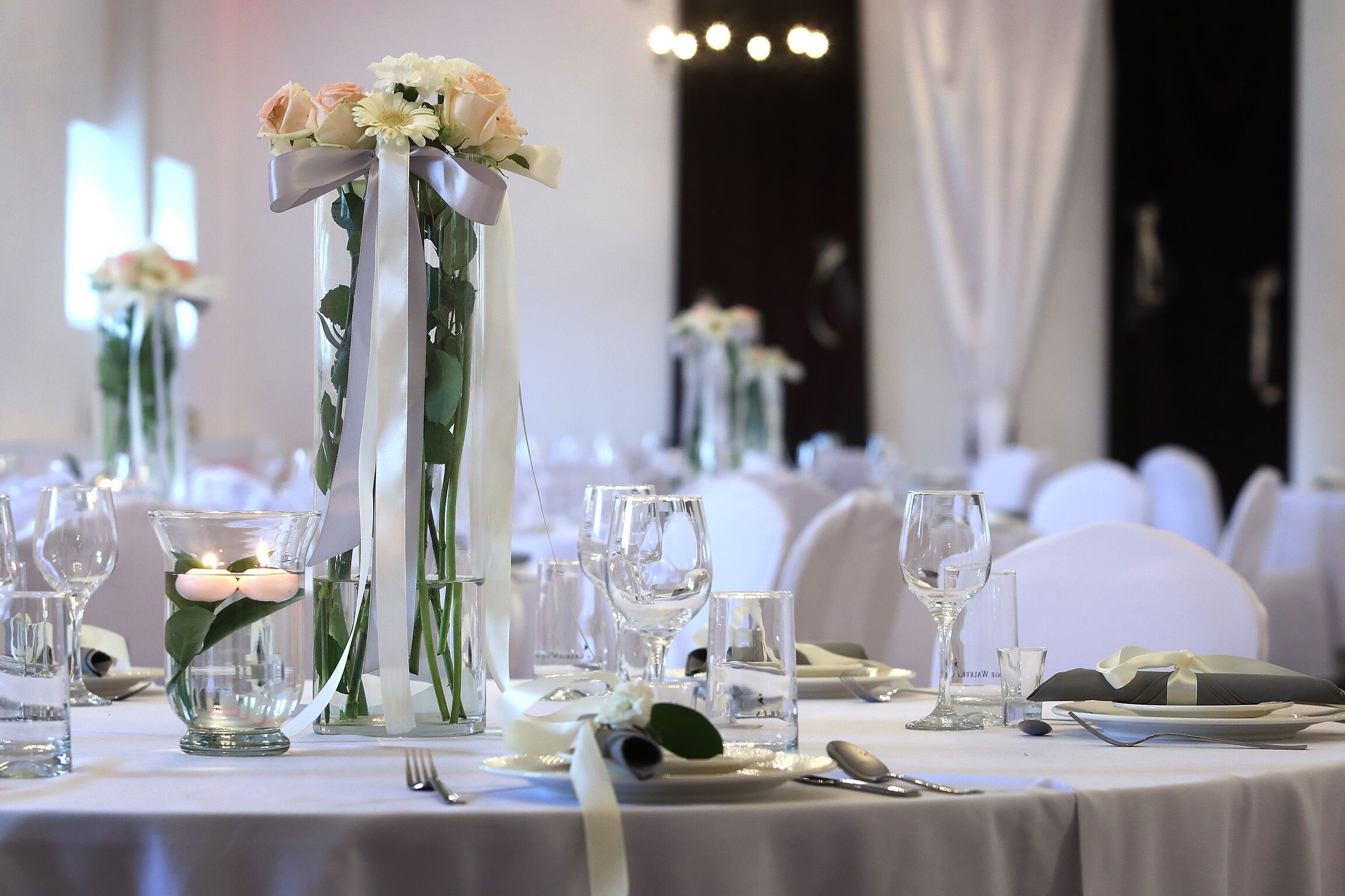 A table set for a formal event with clear glassware, white tablecloths, and floral centerpieces.