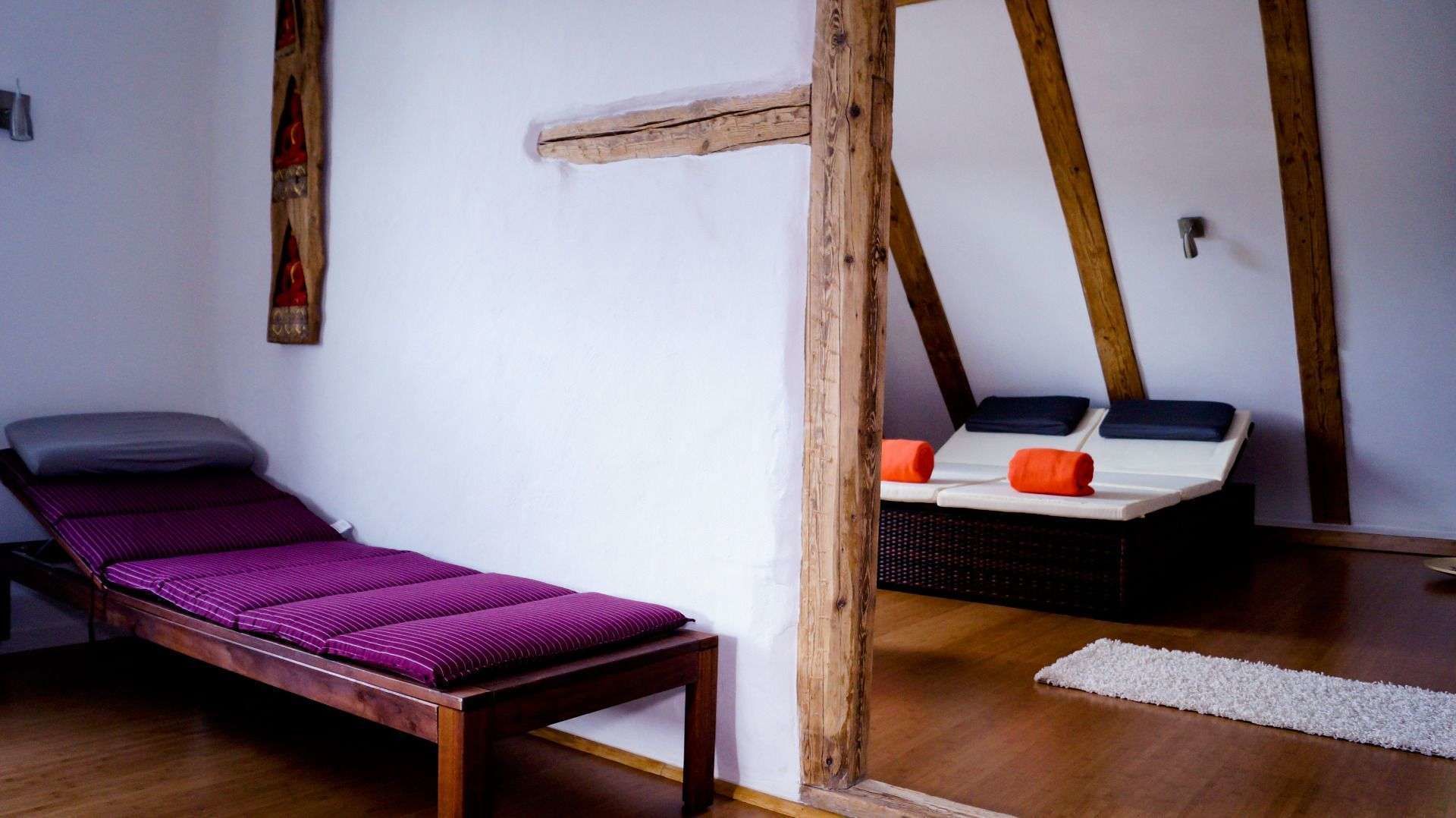 A room with a wooden bed, a small table, and a bench with cushions.