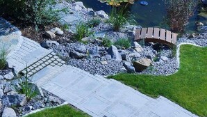 Un jardin avec un chemin pavé, un pont en bois et un étang parsemé de nénuphars.