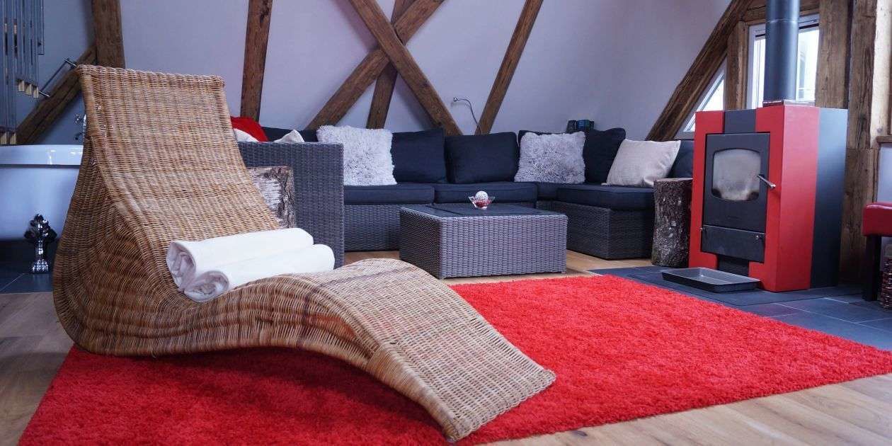 Una sala de estar acogedora con techo alto, alfombra roja, una butaca tejida, un conjunto de sofás y una estufa de leña.