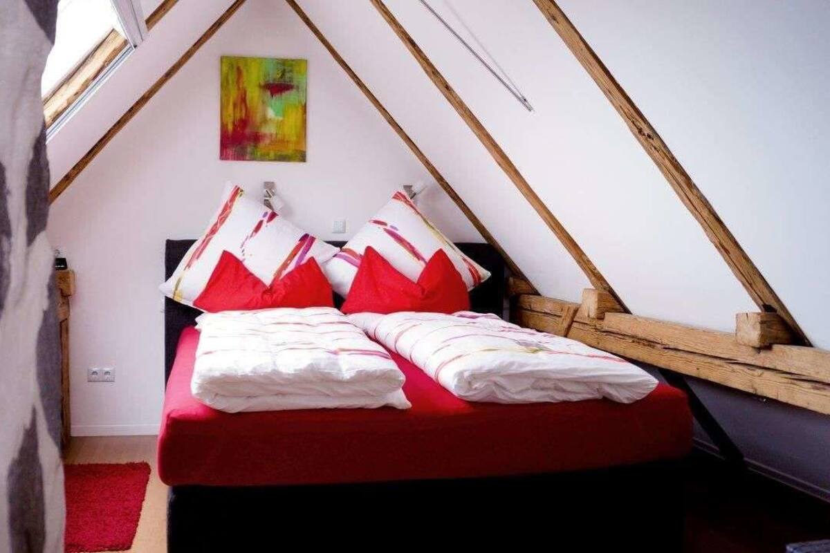 Una habitación pequeña y triangular con una cama, almohadas y un cuadro en la pared.
