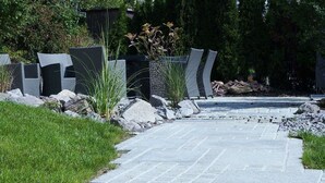 Un chemin pavé mène à un espace aménagé avec des chaises modernes et une petite plante.