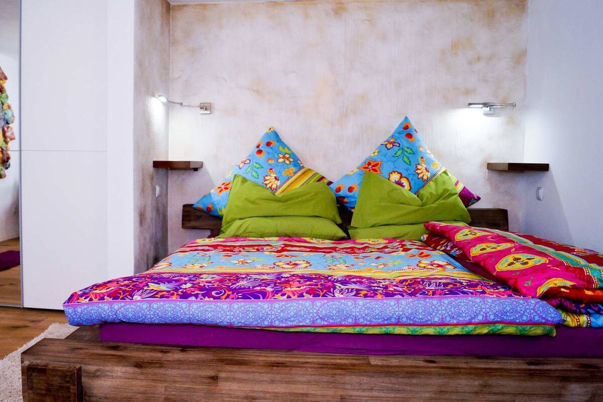 Un dormitorio con una cama de madera, almohadas coloridas y un espejo en la pared.