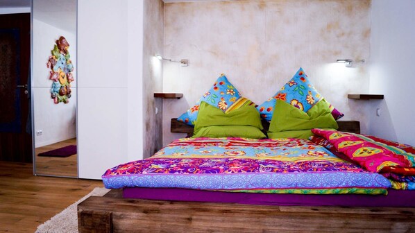 A bedroom with a wooden bed, colorful pillows, and a mirror on the wall.