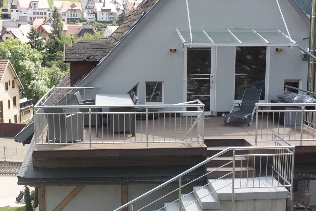 A residential building with a rooftop deck, a glass door leading to a covered outdoor area, and a staircase.