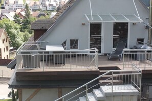 A residential building with a rooftop deck, a glass door leading to a covered outdoor area, and a staircase.